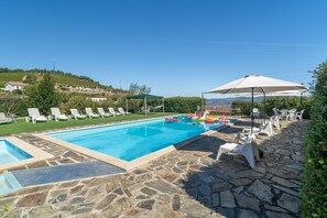 A swimming pool with lounge chairs and umbrellas, surrounded by stone flooring and greenery. - Casa da Jesus with Mountain View, Wi-Fi, and Air Conditioning (Provesende)