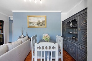 A dining area with a table, chairs, a painting on the wall, a cabinet, and a sofa.
