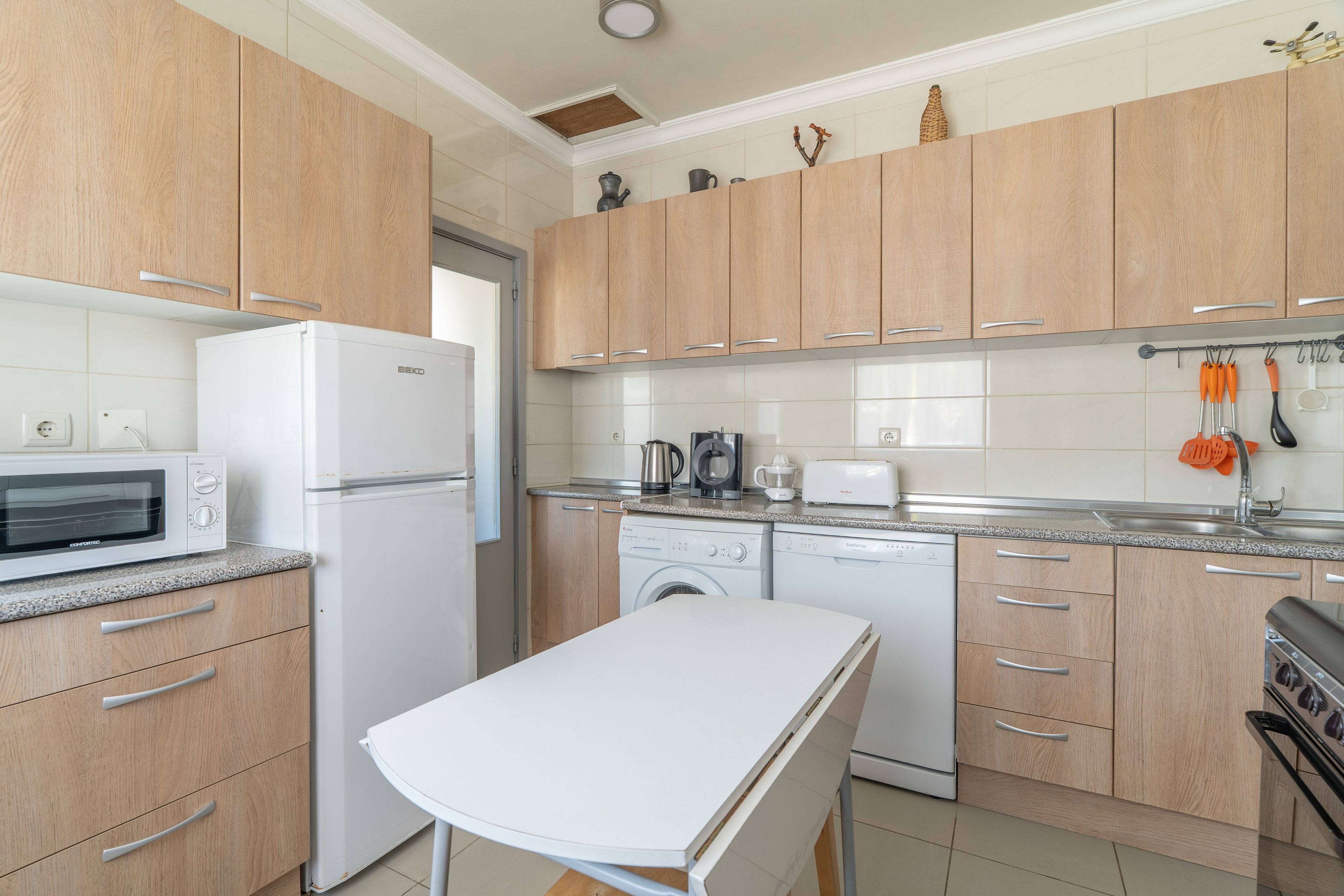 Una cocina moderna con armarios de madera, encimera blanca, horno empotrado, microondas, cafetera, tostadora y lavavajillas.
