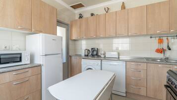 Una cocina moderna con armarios de madera, encimera blanca, horno empotrado, microondas, cafetera, tostadora y lavavajillas.