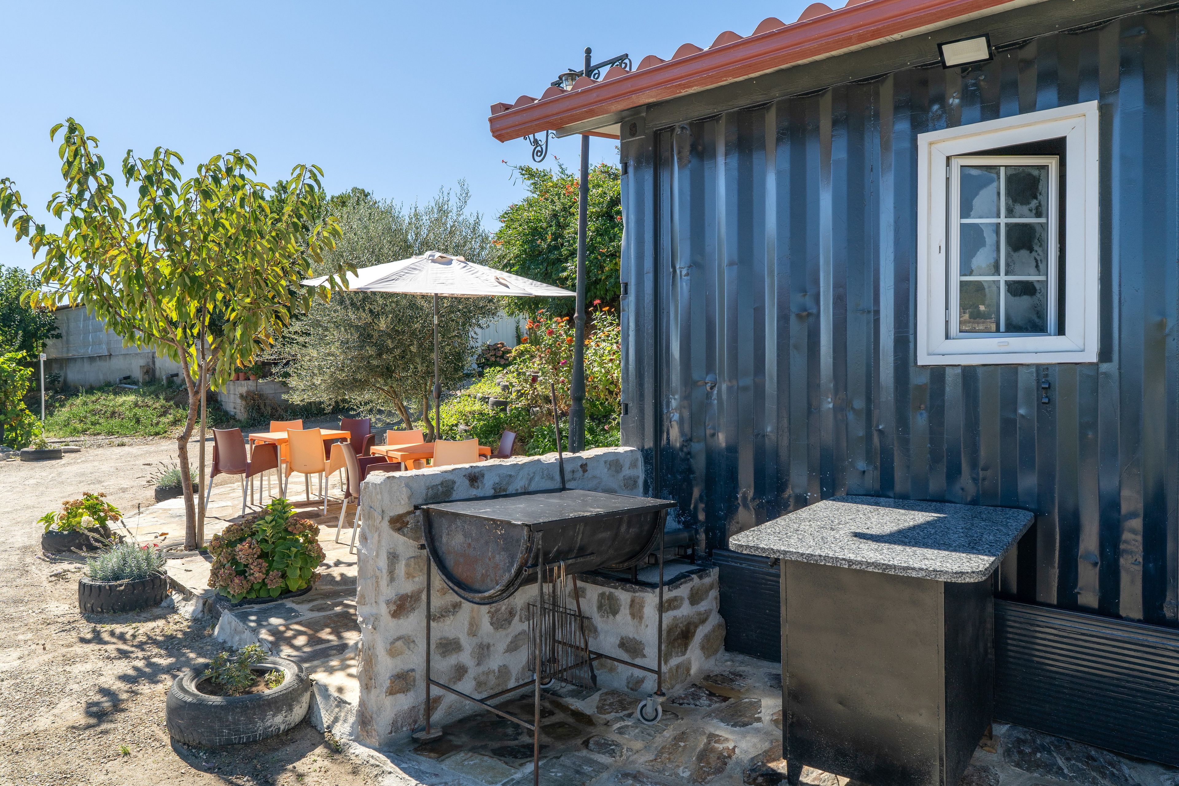 A rustic outdoor seating area with stone tables and chairs, a barbecue grill, and a small shed with a window.