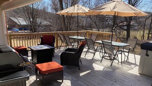 Un patio in legno con mobili da esterno, tra cui sedie e tavoli, e due ombrelloni.