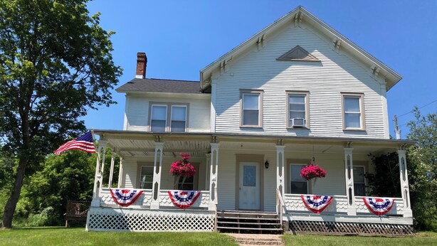 Una casa a due piani con un portico, un camino e una bandiera americana.