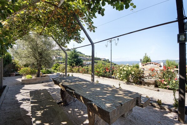 A covered outdoor seating area with a bench, surrounded by gravel and potted plants.