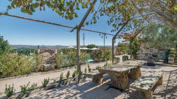 A stone bench under a pergola with a view of a pool and garden.