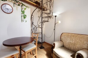 A room with a round wooden table, a sofa, a wall clock, and a decorative metal spiral staircase. - Romantic Room – mountain view, Wi-Fi and air conditioning (Provesende)
