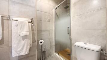 Une salle de bain avec une douche à parois de verre, des toilettes et un porte-serviettes avec des serviettes blanches.