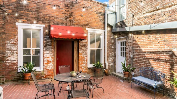 A brick courtyard with a red awning, a round metal table with chairs, and a bench.