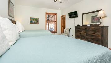 A bedroom with two beds, a ceiling fan, a wooden dresser, and a television displaying 'ABSOLUTE CHARM LUXURY ACCOMMODATIONS'.