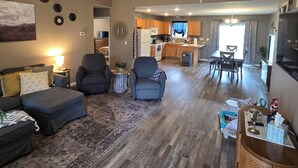 A spacious living room with a ceiling fan, a large rug, and a dining area with wooden furniture. - Blue Sage Inn-Pet Friendly home in Saint Robert, MO. Close to Fort Leonard Wood. (Saint Robert)