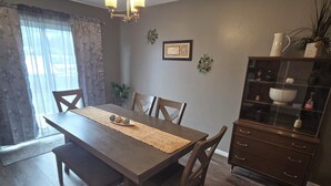 A dining area with a wooden table, chairs, a bench, a chandelier, a cabinet with decorative items, and a window with curtains. - Blue Sage Inn-Pet Friendly home in Saint Robert, MO. Close to Fort Leonard Wood. (Saint Robert)
