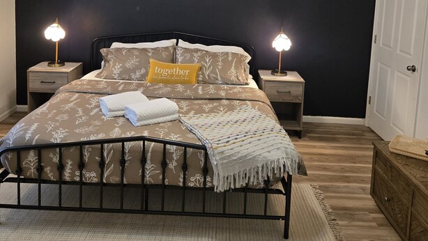 A bedroom with a bed, bedside lamps, a ceiling fan, a framed picture, and a door. - Blue Sage Inn-Pet Friendly home in Saint Robert, MO. Close to Fort Leonard Wood. (Saint Robert)