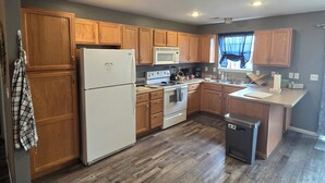 A kitchen with wooden cabinets, a white refrigerator, a microwave, and a dishwasher. - Blue Sage Inn-Pet Friendly home in Saint Robert, MO. Close to Fort Leonard Wood. (Saint Robert)