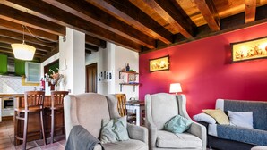 Un salon avec deux fauteuils, un canapé, un coin repas avec une table et des chaises, et une cuisine à l’arrière-plan.