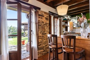 Una cocina rústica con paredes de piedra, sillas de madera y un ventanal con vistas a un jardín.