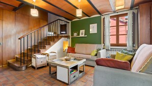 Una sala de estar con una escalera, un sofá, una mesa de centro y un ventanal con cortinas.