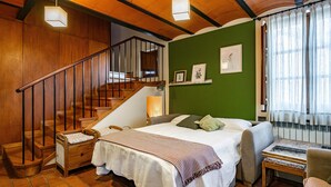 Una habitación con una cama, una silla, una mesita, una escalera y una pared verde.