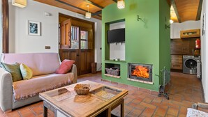Un salón acogedor con chimenea, un sofá, una mesa con una cesta y una zona de cocina con lavadora.