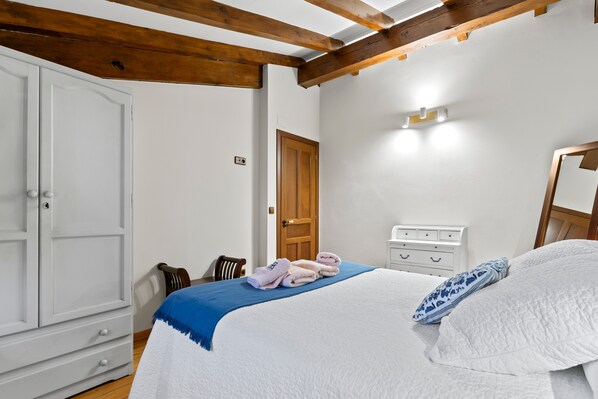 A bedroom with a bed, a wardrobe, a wooden ceiling, a door, and a bedside table.