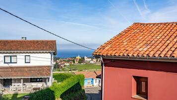 A residential area with a red building, a white building with a tiled roof, and a view of the sea.