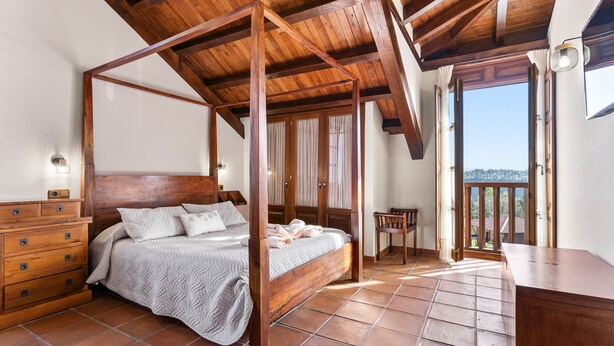 Une chambre à coucher avec un lit à baldaquin en bois, une commode et une vue sur l’extérieur.