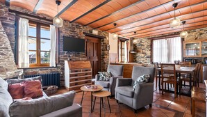 Un intérieur chaleureux avec des murs en pierre, une cheminée, un coin repas et un téléviseur fixé au mur.