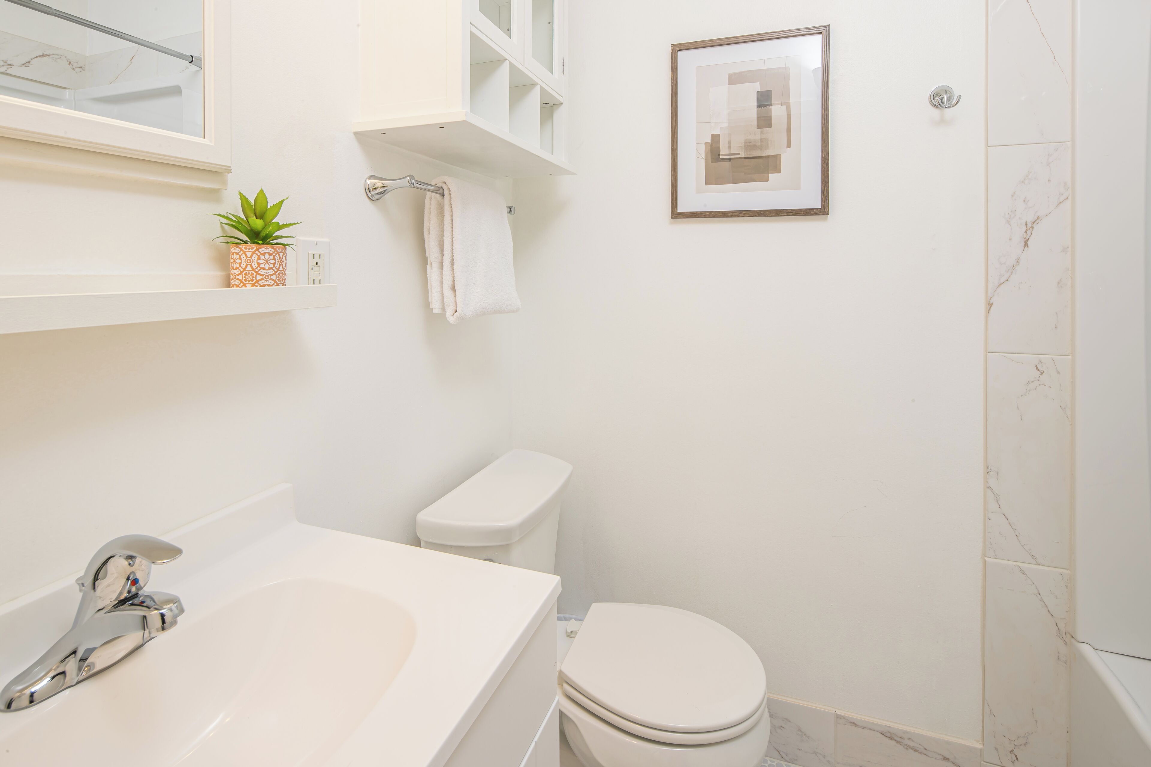 A modern bathroom with a bathtub, toilet, and a framed artwork on the wall.