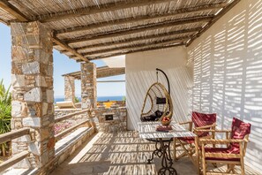 Een stenen terras met een tafel en stoelen, een hangstoel en uitzicht op zee.