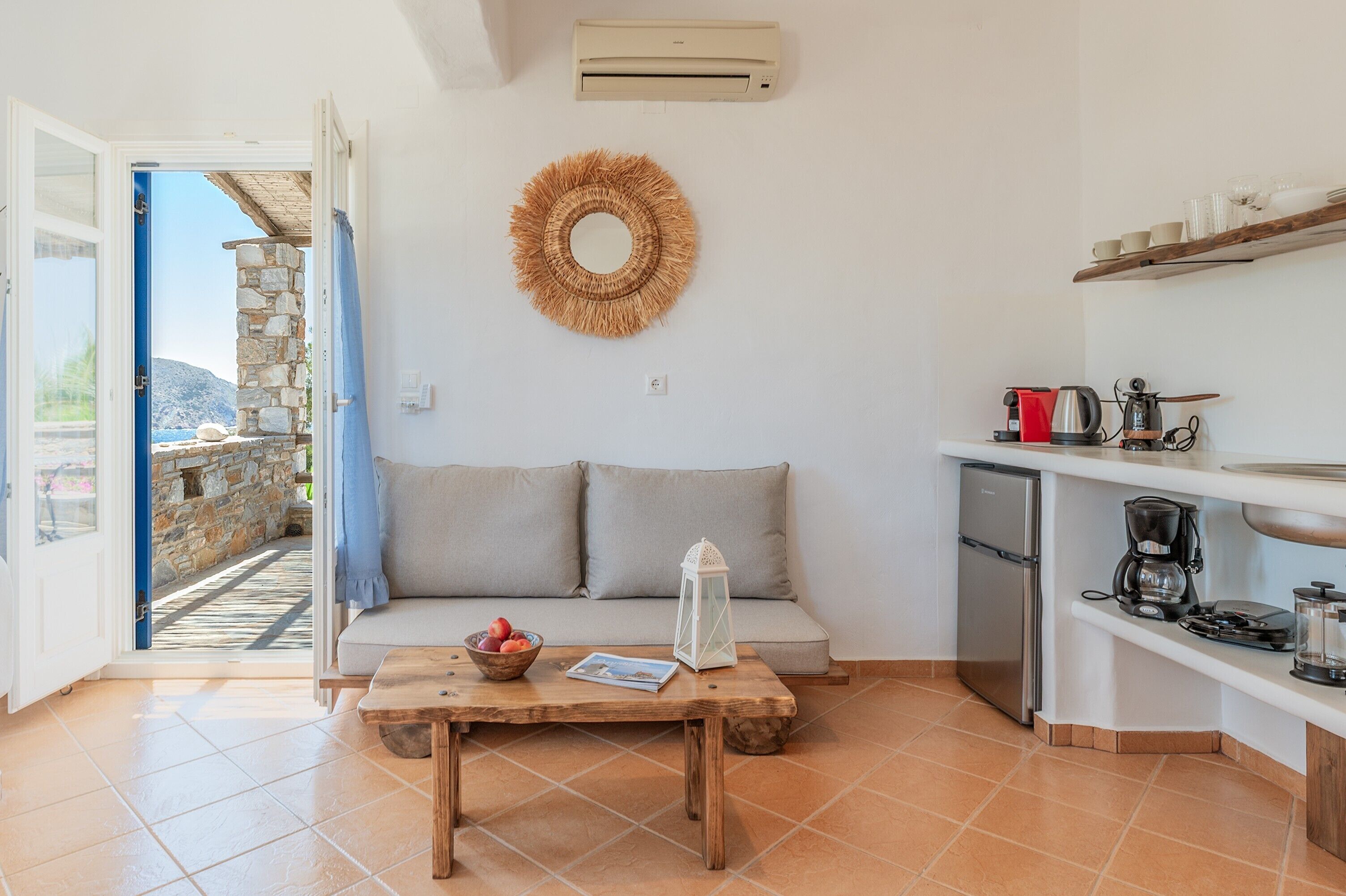 Una sala de estar acogedora con sofá, mesa de centro y una zona de cocina con refrigerador, cafetera y estantes.