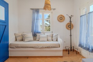 Een slaapkamer met een bed, een raam, een blauwe deur en een kapstok.