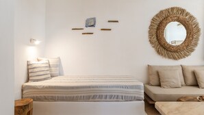 Ein Schlafzimmer mit einem Bett, einem Schlafsofa, einem runden gewebten Spiegel und einer Wandleuchte.