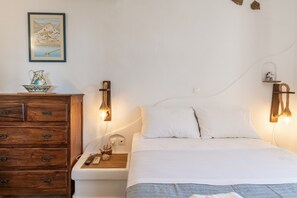 A bedroom with a bed, wooden dresser, bedside lamps, and a wall-mounted shelf. - Apartment 'Suite No 4' with Sea View, Wi-Fi and Air Conditioning (Kini)