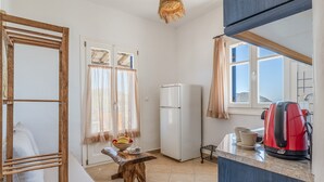 A compact kitchen with a refrigerator, a wooden bench, a table with a fruit bowl, and a red kettle on the counter. - Apartment 'Suite No 4' with Sea View, Wi-Fi and Air Conditioning (Kini)
