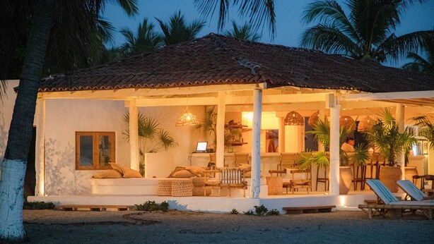 A beachfront villa with a tiled roof, a covered outdoor seating area, and a poolside lounge.