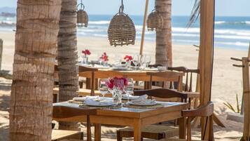 Un conjunto de comedor exterior de madera con mesas y sillas, rodeado de palmeras y vistas a la playa.