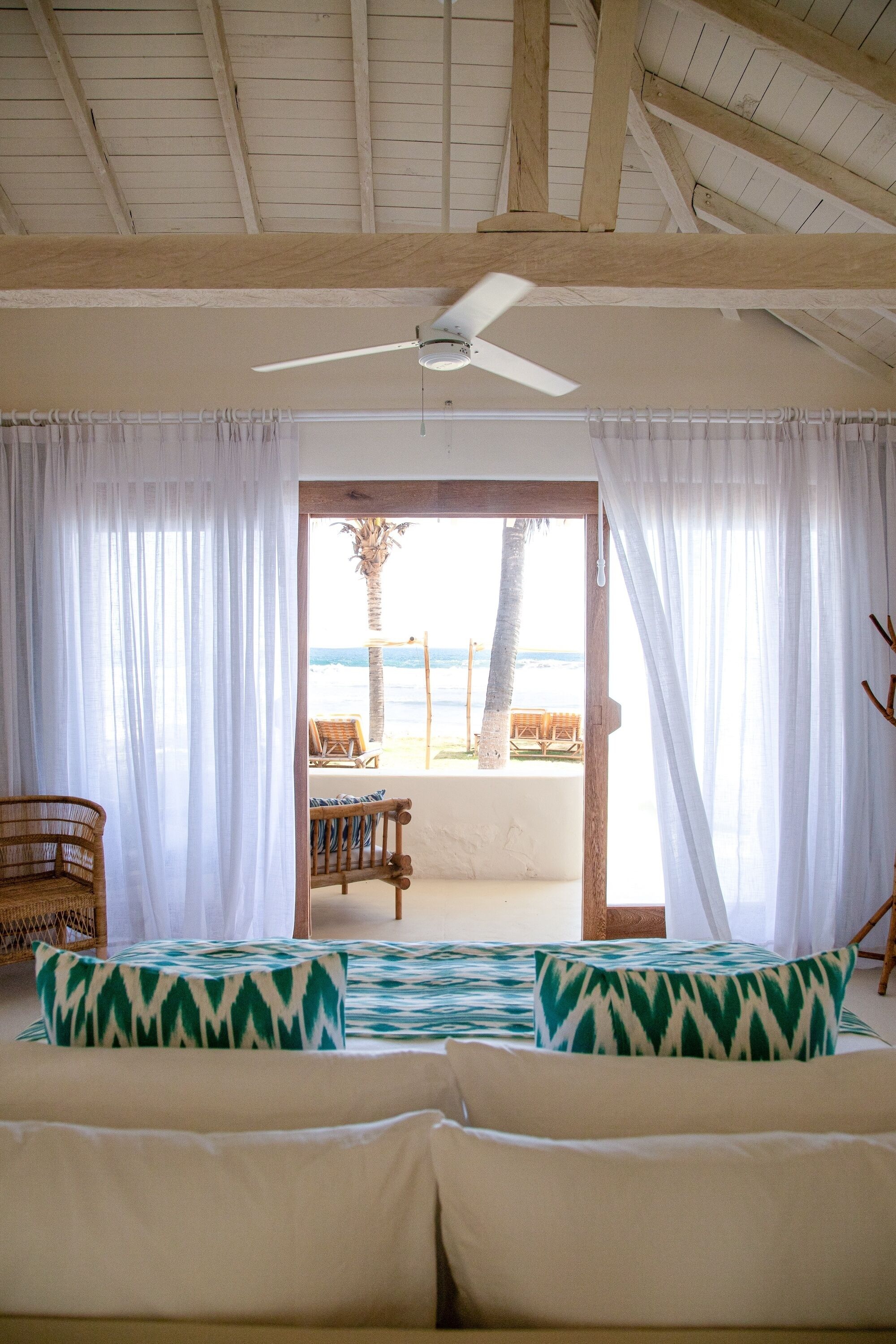 A room with a bed, a ceiling fan, and a view of the beach through a doorway.