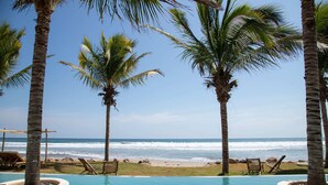 A pool area with palm trees, beach chairs, and a view of the ocean.