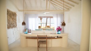 A beachside room with a curved white counter, a wooden chair, and a view of the ocean through large windows.