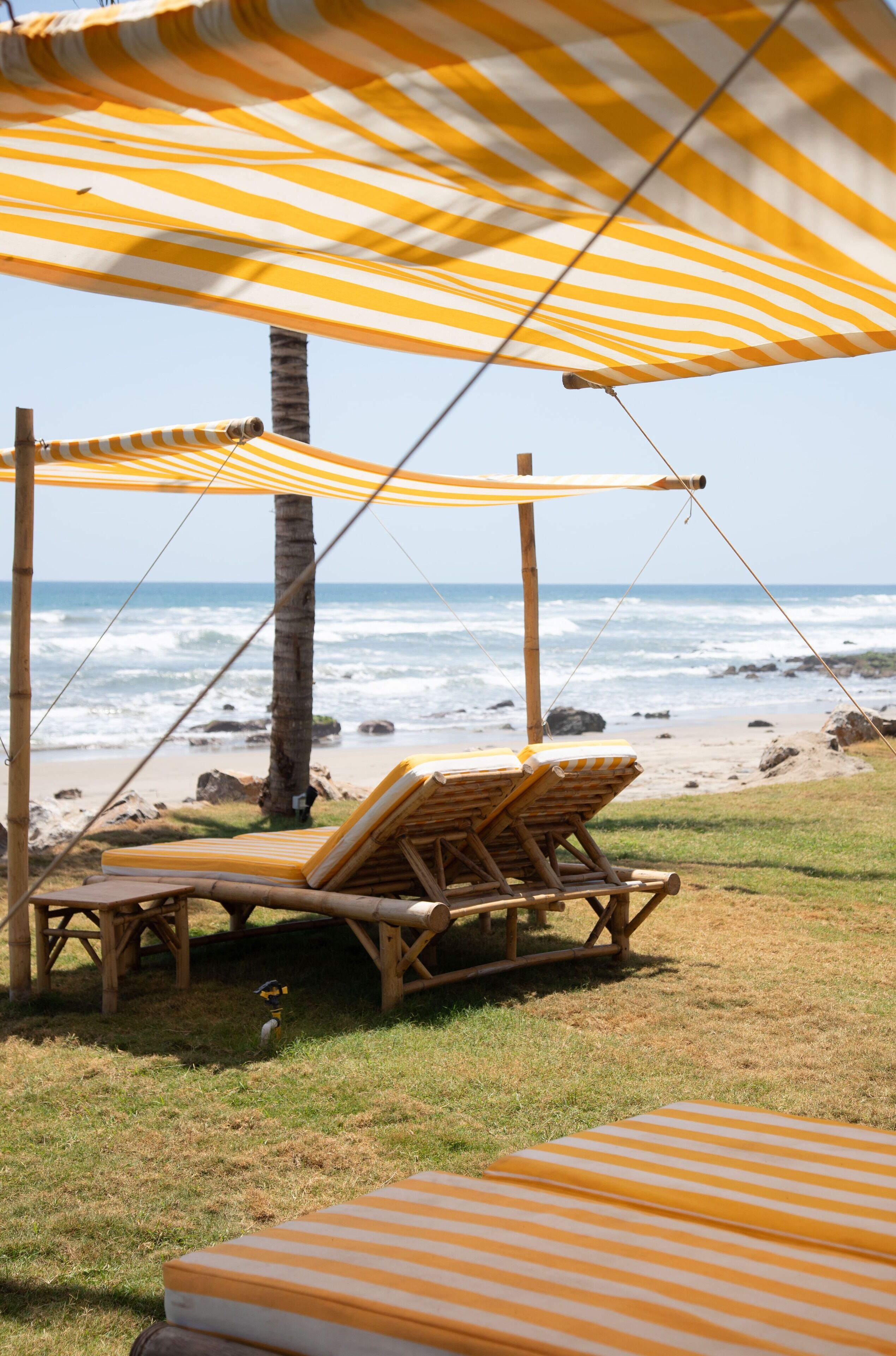 A beachside lounge area with striped canopies and wooden lounge chairs.