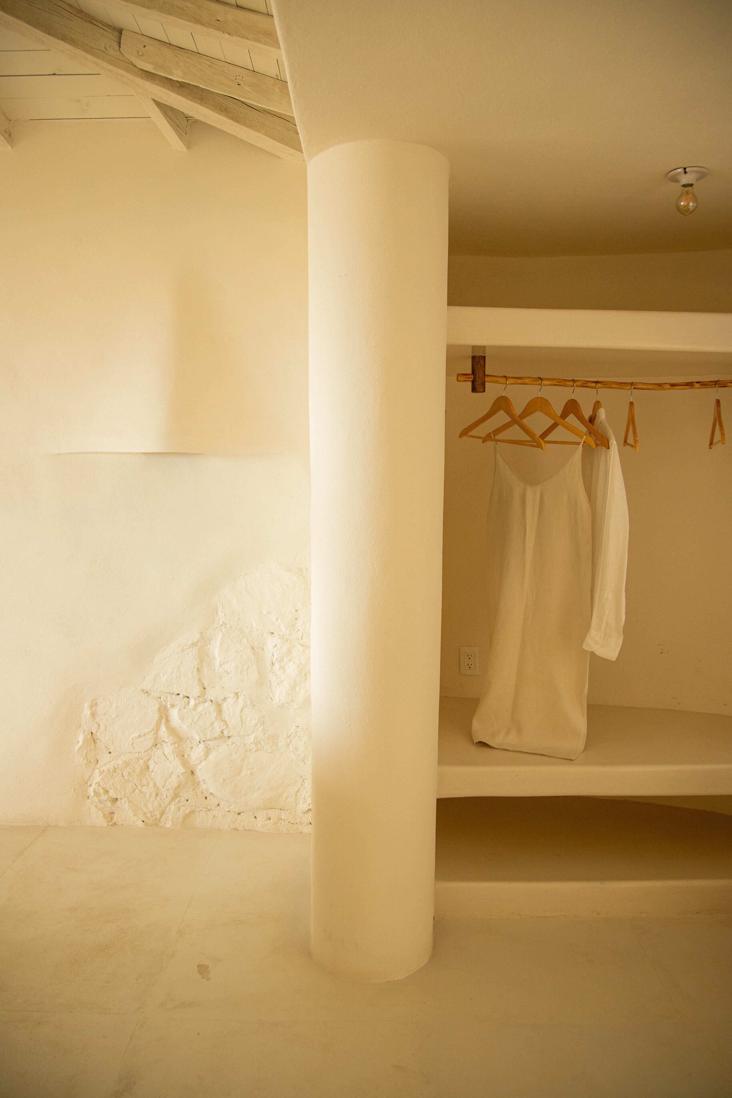 A room with a white column, a hanging garment, and a shelf.