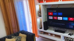 Ett modernt vardagsrum med en svart soffa, ett soffbord i glas och en tv på ett vitt tv-bord, ovanför vilket det finns en röd skylt med bokstaven "E".