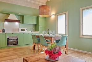 Une cuisine avec des meubles de rangement verts, une table à manger avec des chaises et un luminaire suspendu.