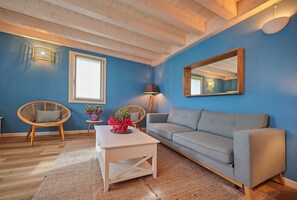 Une pièce avec un mur bleu, un canapé gris, une table basse blanche, deux fauteuils en osier, un miroir et une lampe.