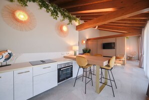 A modern kitchen with white cabinetry, a wooden dining table with bar stools, and decorative wall sconces. - Apartment 'Ca' Marano Lagoon' with Shared Pool, Wi-Fi and Air Conditioning (Località Bevazzana)