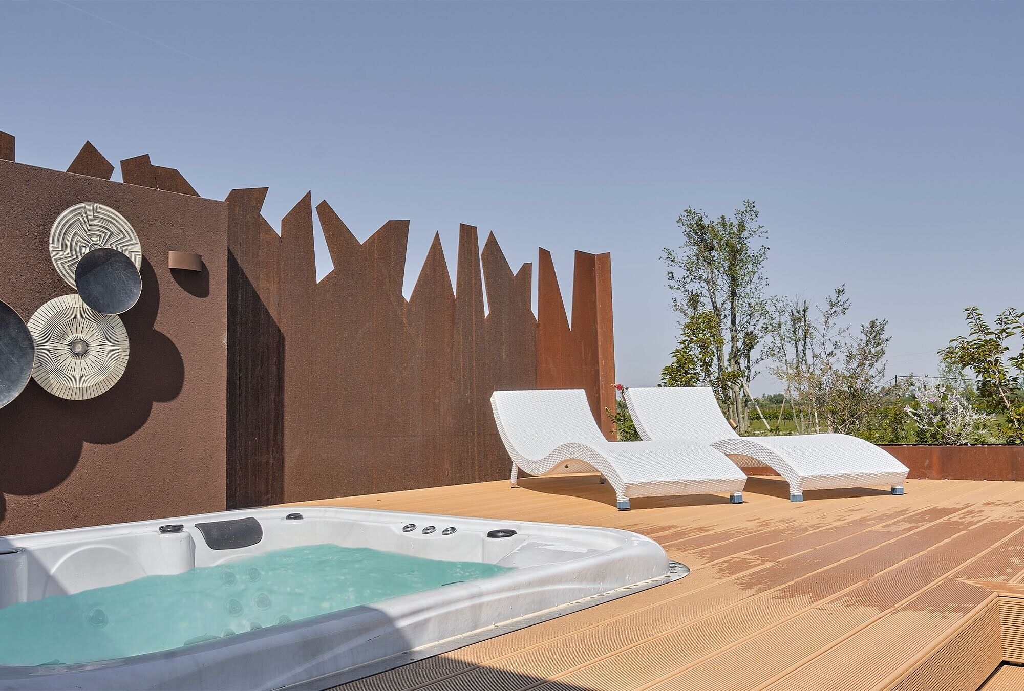 A hot tub with two lounge chairs, a decorative wall, and a clear sky.