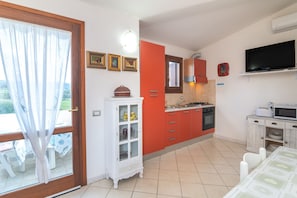 A kitchen with a dining area, a TV, and a window with curtains. - Holiday Home 'Bouganville' with Mountain View, Private Garden and Air Conditioning (Posada)