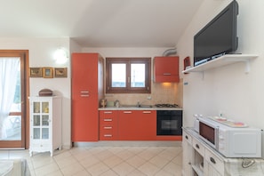 A compact kitchen with a microwave, oven, and a TV mounted above the counter. - Holiday Home 'Bouganville' with Mountain View, Private Garden and Air Conditioning (Posada)