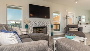A modern living room with a fireplace, grey sofas, a flat-screen TV, and a view of the outdoors.