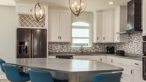A modern kitchen with a large island, stainless steel appliances, and blue bar stools.