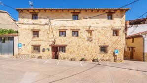 Un edificio de piedra con techo plano, varias ventanas y un estacionamiento.